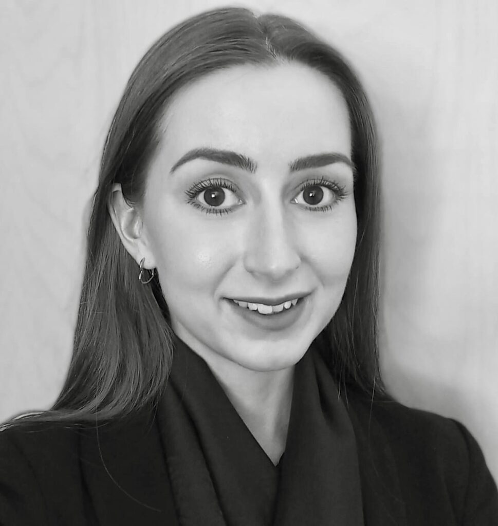A monochromatic portrait of a smiling young woman with long hair, wearing a blazer and subtle earrings, exuding a professional and friendly demeanor.
