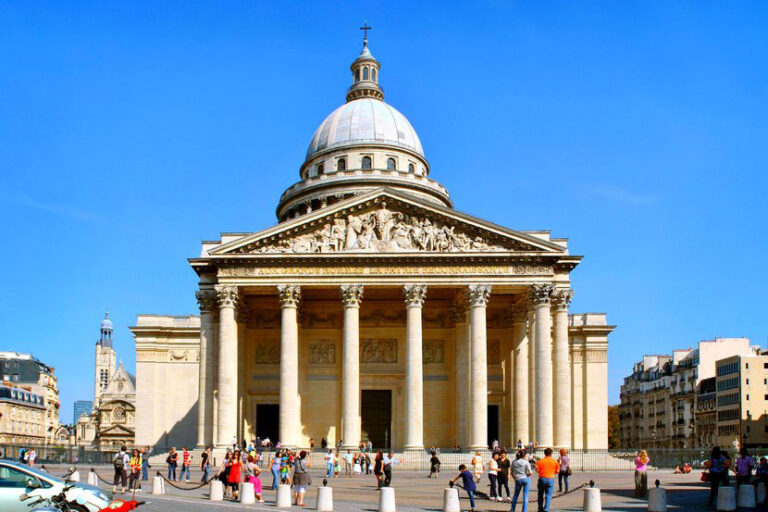 Etunäkymä Pariisin Panthéonista, jossa on upea uusklassinen julkisivu kuudella korinttilaisella pylväällä, jotka tukevat päällystä. Suuri kupoli on rakenteen merkittävä piirre. Turisteja nähdään kokoontuneena sisäänkäynnille aurinkoisena päivänä kirkkaalla sinisellä taivaalla.  